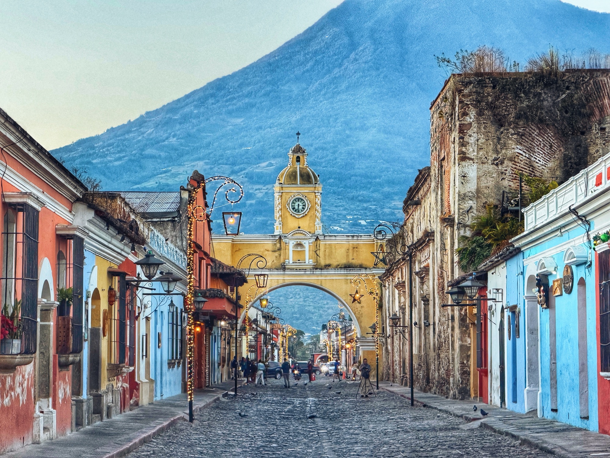 Cobblestone street in Antigua Guatemala lined with colonial buildings, with a volcano visible in the background